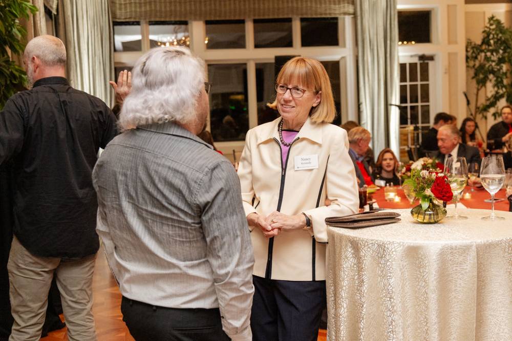 Nancy Kennedy leaning gently on one of the decorated tables, speaking with other party guest